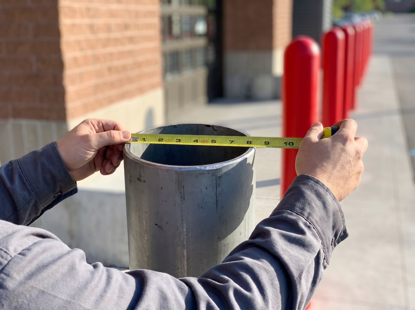 Tape measure held across the open top of a bare steel bollard pipe, outside edge to outside edge